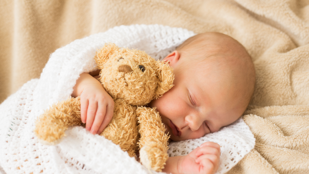 infant sleeping and holding a teddy bear